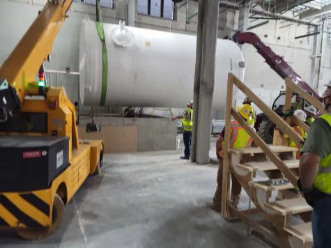 MEI Industrial Solutions crew operating a crane and forklift to hoist a fiberglass waste tank indoors