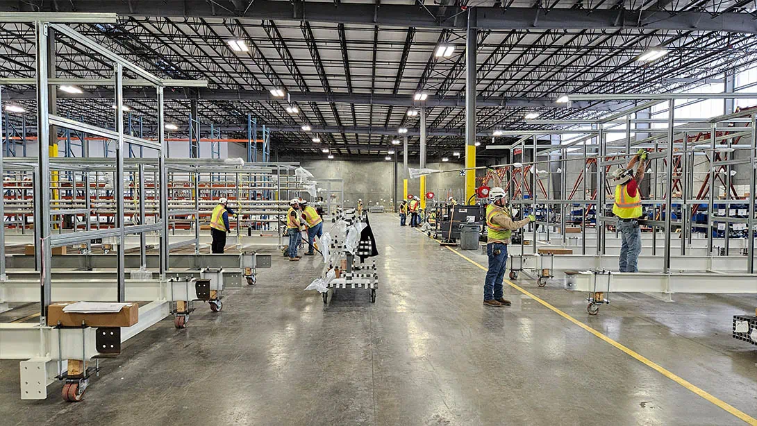 MEI Industrial Solutions millwright technicians in hard hats and safety vests assembling modular steel framing structures inside MEI's warehouse.